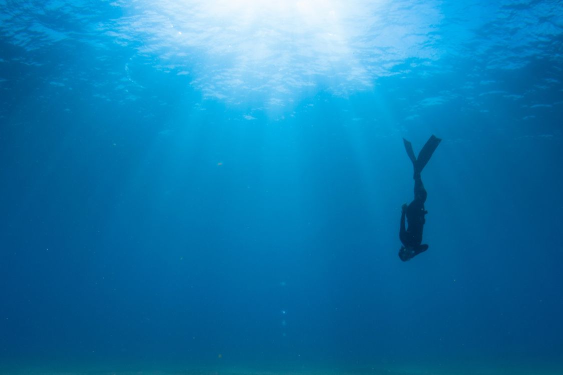 Freediver Hanli Prinsloo swimming towards the ocean floor with sun rays shining through the surface